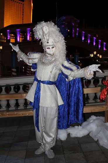 Person in white and blue costume with a feathered headdress poses outdoors at night.