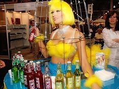 Woman in yellow costume surrounded by bottles of soda at a booth.