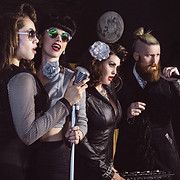 Group of four people, two women with microphones singing, two others beside them, possibly musicians.