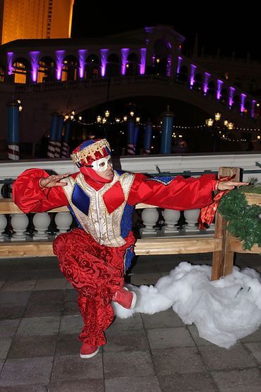 Person in a red and blue jester costume poses near a bridge at night.
