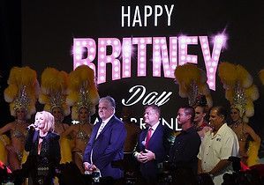A group of people are standing in front of a large screen that says happy britney day.