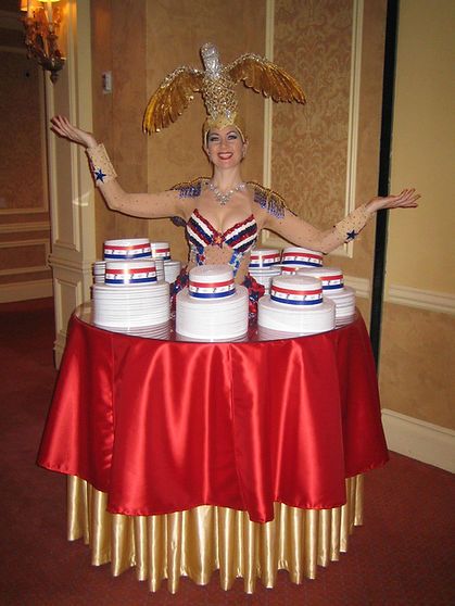 Woman dressed as an eagle with a table of cakes in red, white, and blue.