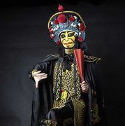 Actor in elaborate Chinese opera costume: black cape, gold trim, yellow mask, holding a red fan.