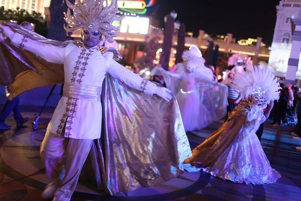 Dancers in white and gold costumes perform at night in a city with bright lights.
