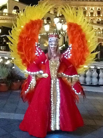 Woman in red and gold phoenix costume with large feathered wings, outdoors at night.