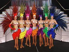 Seven showgirls in colorful costumes with feather headdresses.