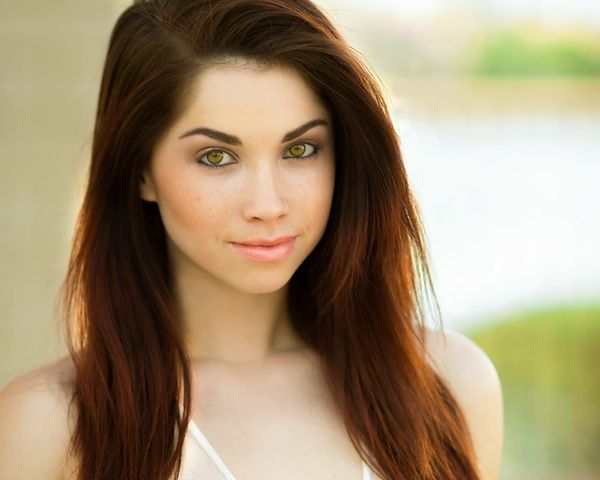 Woman with long red hair and green eyes, smiling, looking at the camera.