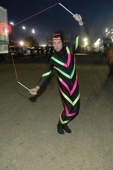 Man in black jumpsuit with neon stripes performs a rope trick outdoors at night.