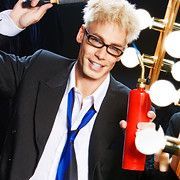 Man with blonde hair and glasses, in suit, holding a fire extinguisher, smiling.