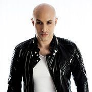 Bald man with dark eyeliner in a black leather jacket and white shirt looking at the camera.