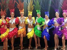 Dancers in vibrant, rainbow-colored costumes with feathered headdresses.