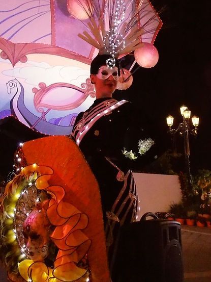 Woman in elaborate costume with mask and lights at night.
