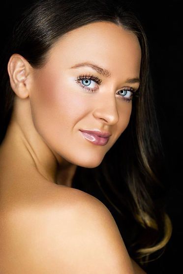 Woman with blue eyes, turned toward the viewer, shoulder exposed. Black background, soft lighting.