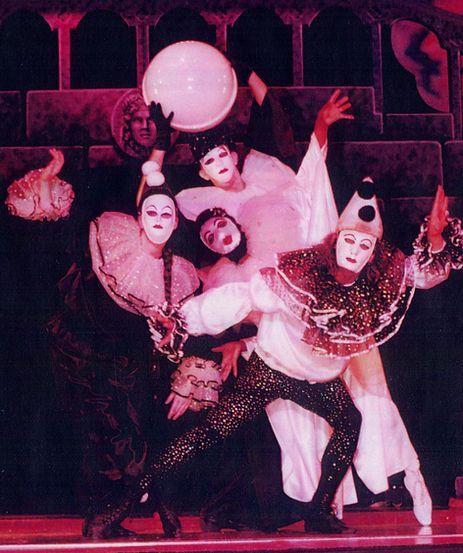 Dancers in elaborate white and black costumes, theatrical setting, holding a white sphere, posing dramatically.