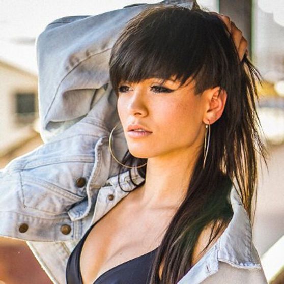 Woman with dark hair and bangs, wearing a denim jacket and black top, looking away.