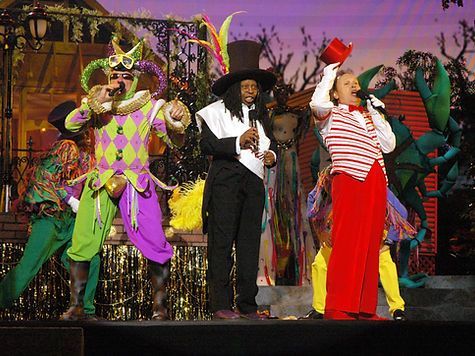 Three people on stage in colorful Mardi Gras costumes; background set.