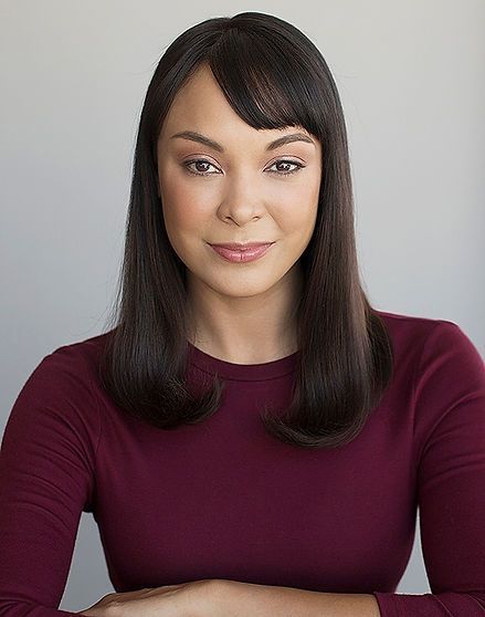 Woman with dark hair and bangs wearing a maroon shirt, smiling at the camera.
