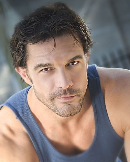 Man in a blue tank top looking at the camera with a serious expression.