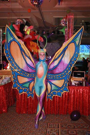 Woman in butterfly costume, brightly colored wings, posing at party with decorations.
