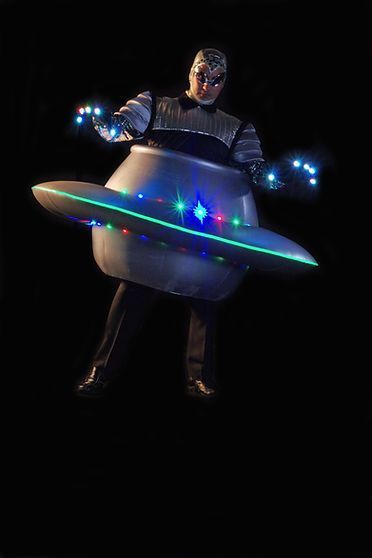 Person in a UFO costume, glowing lights, dark background.