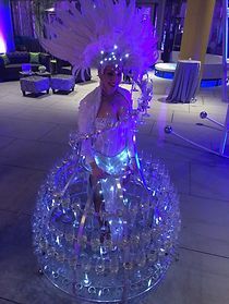 A woman in a feathered hat is standing on a tray of champagne glasses.