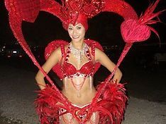 Woman in elaborate red costume with heart-shaped accents, smiling, outdoors at night.