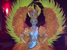 Woman in elaborate orange and yellow feathered costume, posing with hands on hips.
