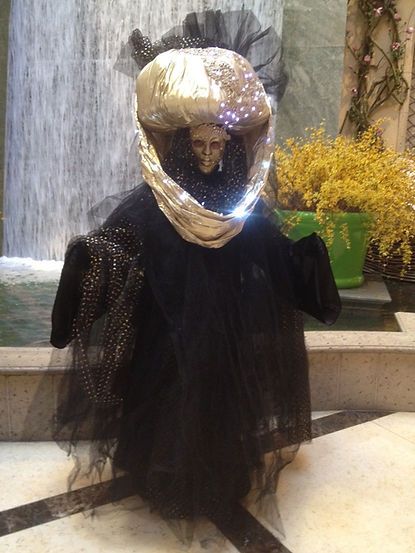 Spooky Halloween decoration: a ghastly figure with a skeletal face wearing a black gown and headdress, lit by small lights.