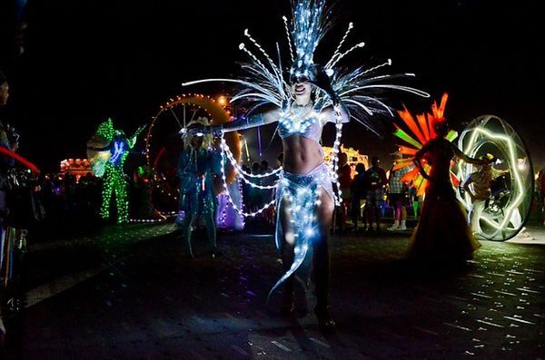 People in illuminated costumes at a night festival. Glittering headdress and lights on their bodies.