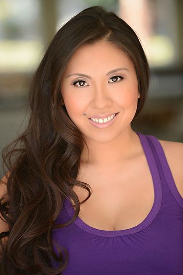 Woman with long brown hair smiles at the camera, wearing a purple tank top.