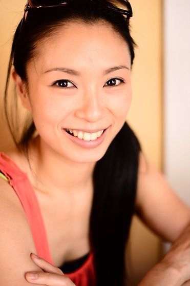 Smiling Asian woman with long dark hair, wearing sunglasses, red top.