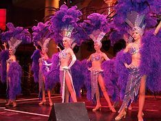 Showgirls in purple feathered costumes perform on stage.