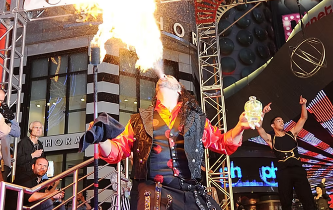 A man is blowing flames out of his mouth in front of a building that has the word hotel on it