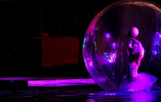 A man is standing inside of a bubble in the water.