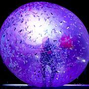 Person inside a large, purple balloon with confetti, lit from within.