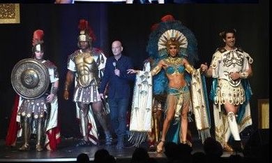 People in Roman costumes and host onstage. Dark background, stage lights.
