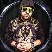 Man wearing sunglasses and a hat with a jacket featuring a pharaoh design, surrounded by a metallic circular border.