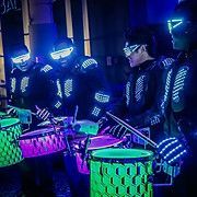 Drummers in illuminated suits and glowing drums, performing at night.