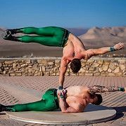 Two men performing acrobatic handstand; one balancing on the other's hands in outdoor setting.