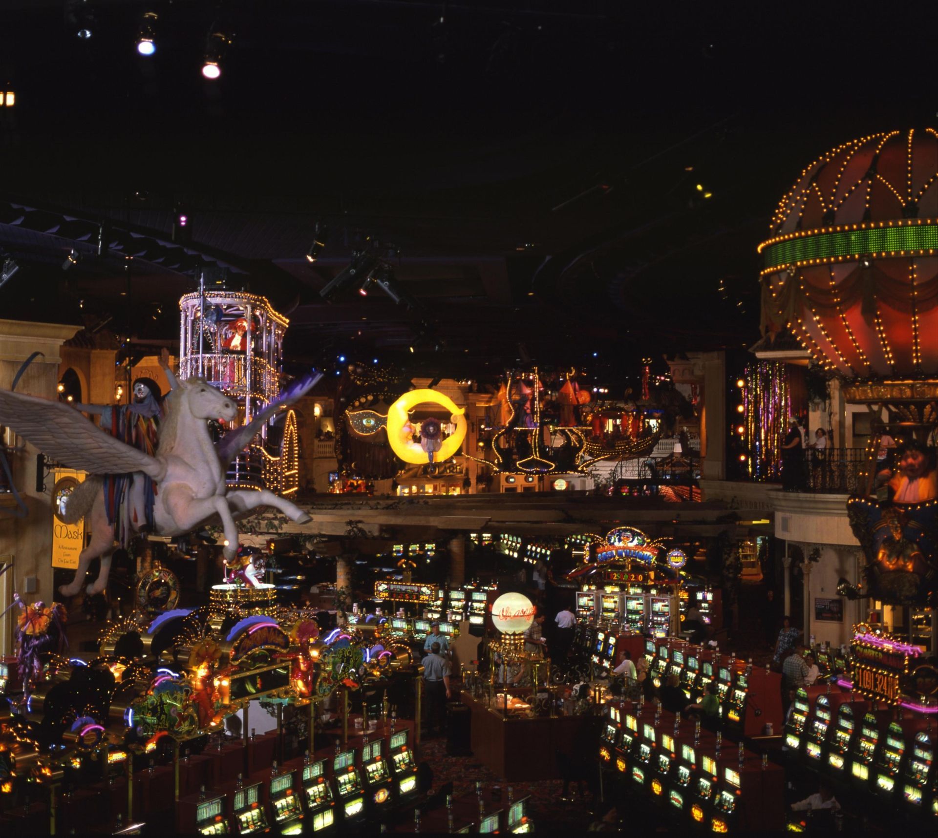 Casino interior with Pegasus statue, slot machines, and elaborate decor at night.
