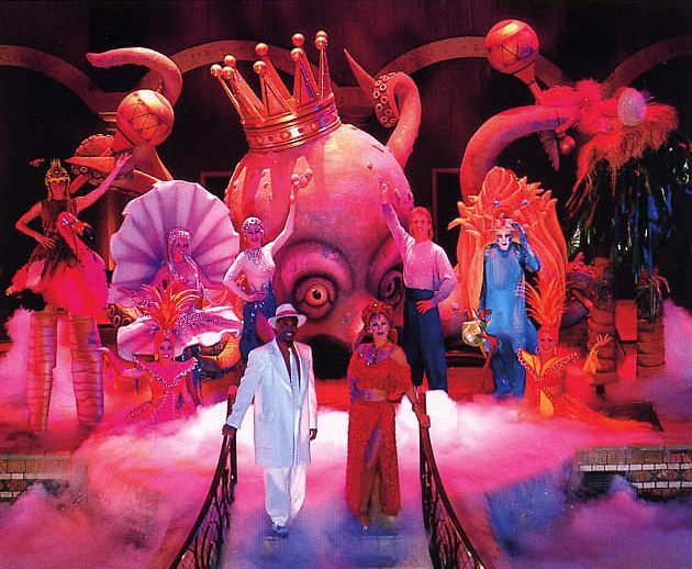 Stage production with performers and fantastical props. A large octopus, a king's crown, and colorful costumes.