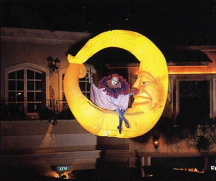 Giant illuminated crescent moon with a clown inside against a building.
