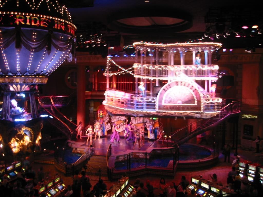 Stage show with dancers on a riverboat and hot air balloon, surrounded by slot machines.