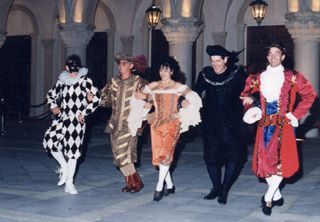Five people in Renaissance costumes dancing in a courtyard with columns.