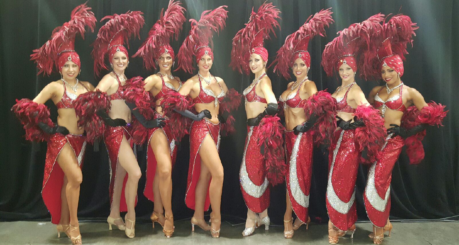 Nine women in red feathered costumes, posing.