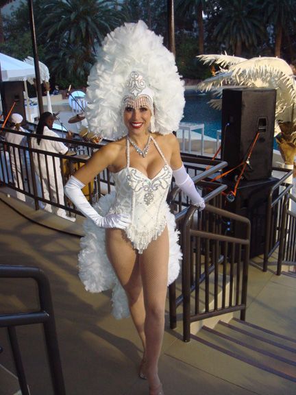 Woman in white showgirl costume smiling near a pool.