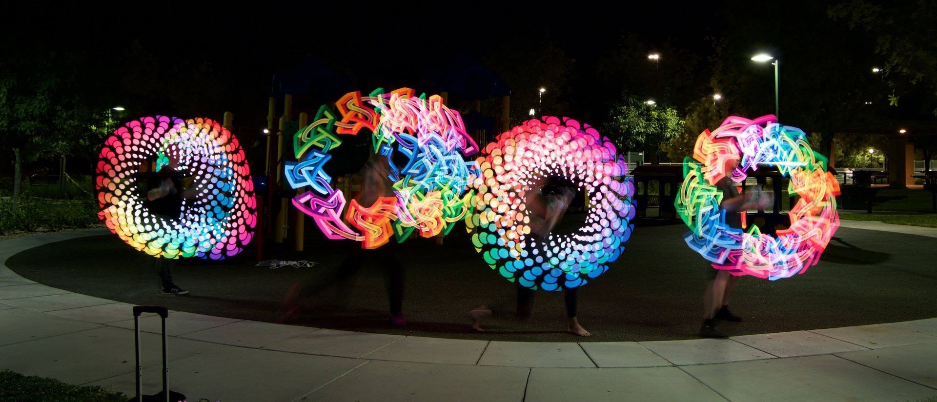 Four people performing with illuminated, colorful, circular LED props at night.