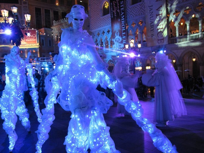 People in glowing white costumes with blue lights, performing on a city street.