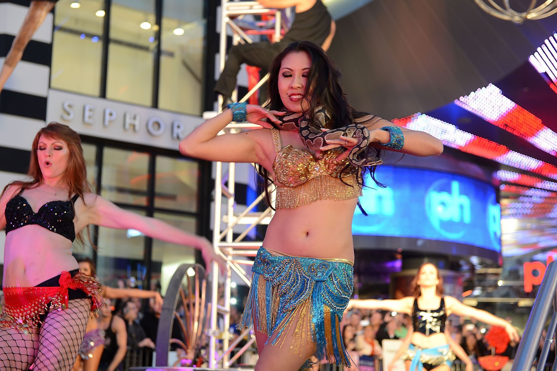 Belly dancers performing on a stage in front of a store, wearing colorful costumes and striking poses.