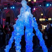 Ice sculpture figure on stilts with blue lights, performing at an outdoor event.